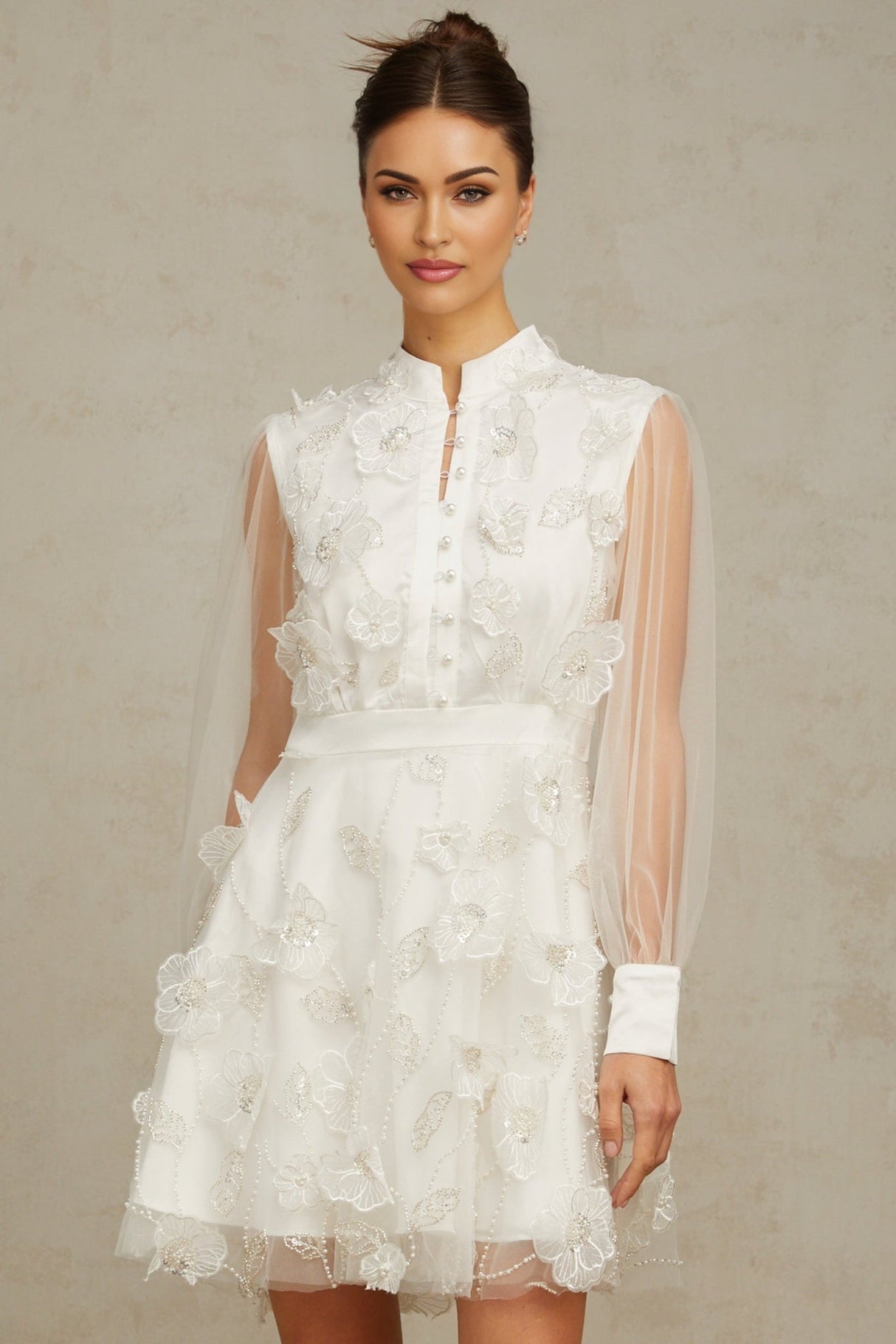 A short white mini dress with a textured 3D petal design made of tulle fabric featuring a floral inspired pattern throughout