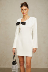 A short white mini dress with an asymmetric hemline featuring a prominent bowknot detail and named Colette