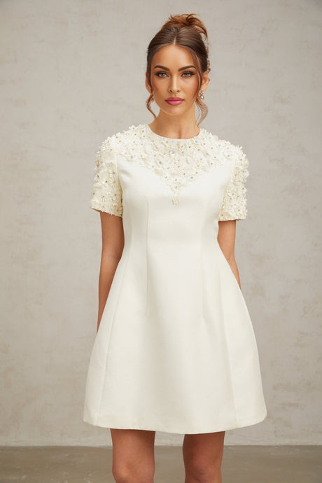 A short white mini dress with colorful floral applique designs scattered across the fabric featuring a fitted bodice and flared skirt