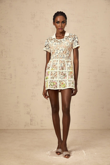A short white mini dress with colorful floral embroidery patterns scattered across the fabric featuring a fitted waist and slightly puffed short sleeves