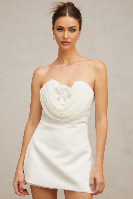 A short white mini dress with floral applique details on a model against a plain background