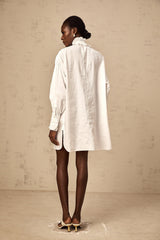 A short white mini dress with lace trim and ruffled details featuring a shirt style collar and buttonup front