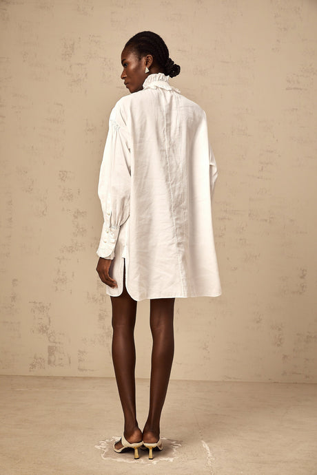 A short white mini dress with lace trim and ruffled details featuring a shirt style collar and buttonup front