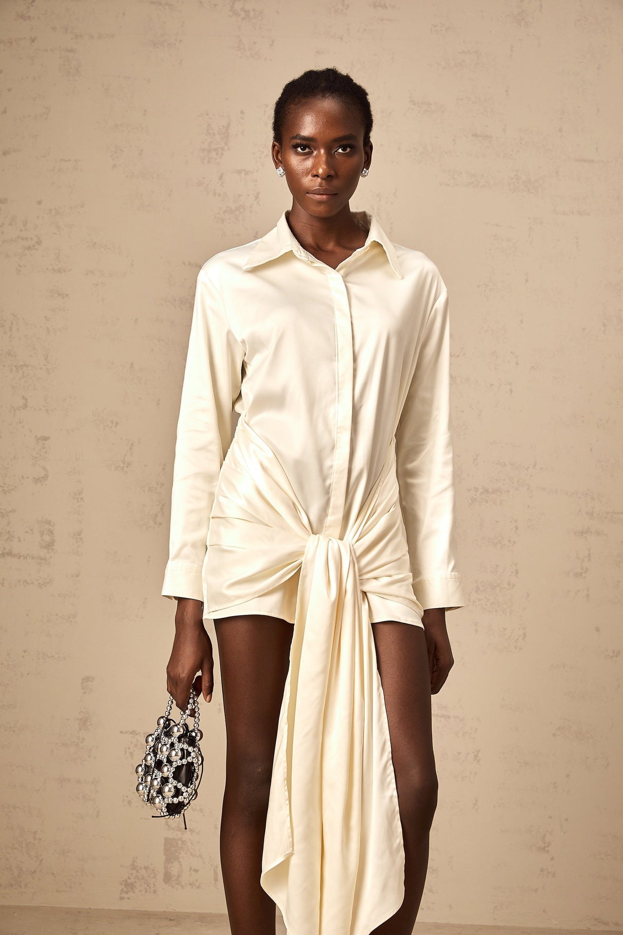 A short white mini dress with ruched details and a ribbon accent featuring a shirtstyle design and called Daphne