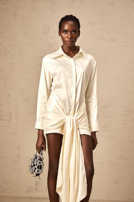 A short white mini dress with ruched details and a ribbon accent featuring a shirtstyle design and called Daphne