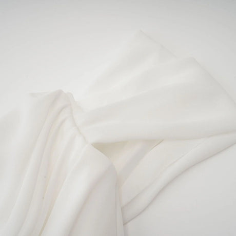 A short white mini dress with ruched fabric and ribbon details on a female model against a plain background