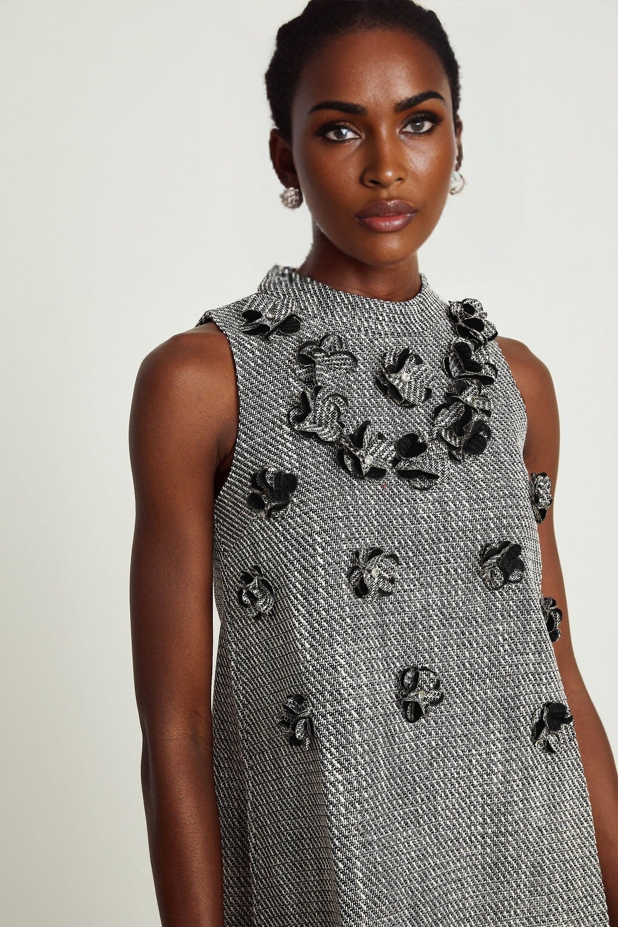 A sleeveless mini dress adorned with faux flowers featuring a floral pattern and short hemline