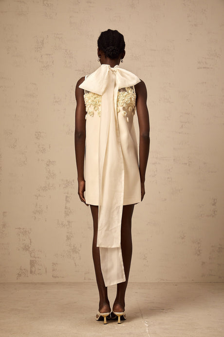 A sleeveless mini dress with faux flower details in a light color against a plain background