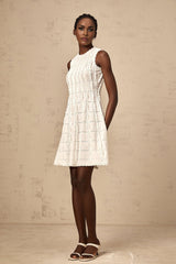 A sleeveless white knit mini dress with ruffled details worn by a model standing against a plain background