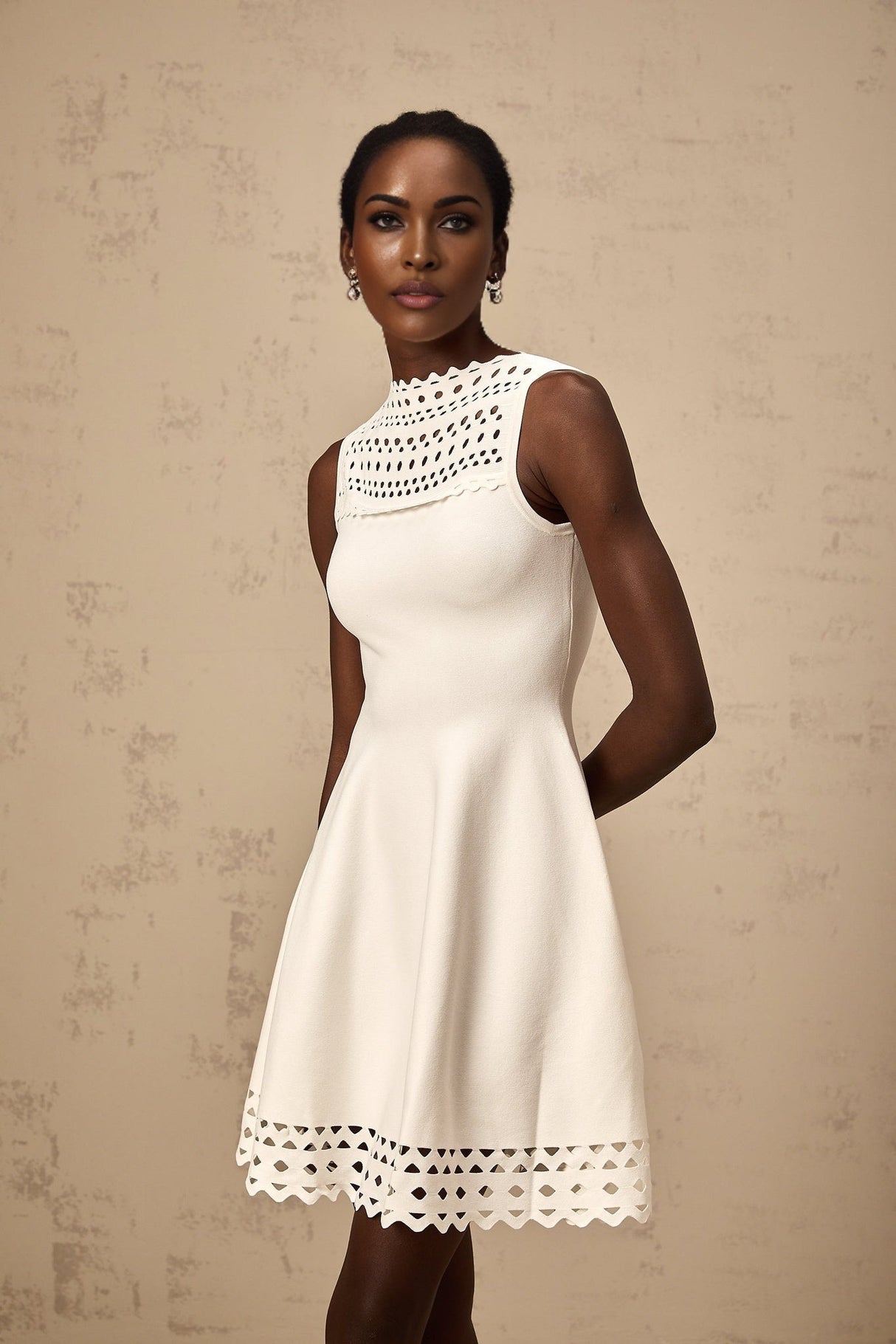A sleeveless white knitted mini dress with cutout details featuring a formfitting silhouette and a short hemline