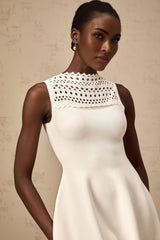 A sleeveless white mini dress with a knitted texture and cutout details worn by a model standing against a plain background