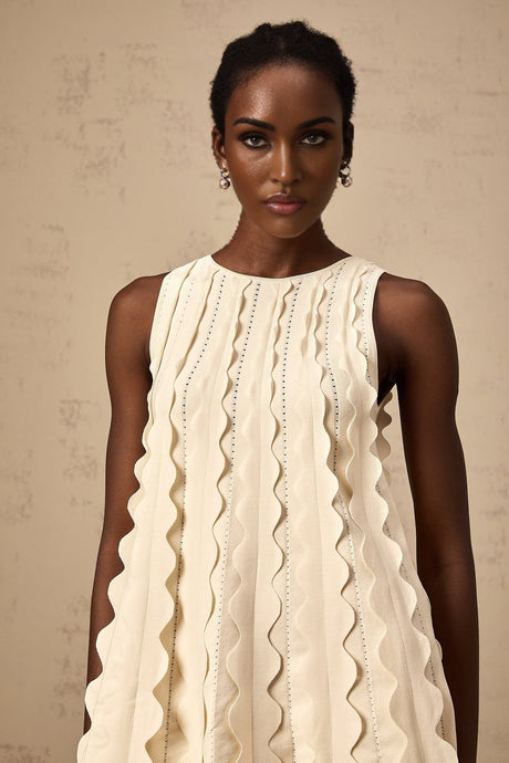 A sleeveless white mini dress with wavy details called Axelle worn by a model standing against a plain background