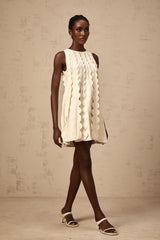 A sleeveless white mini dress with wavy details named Axelle on a plain background
