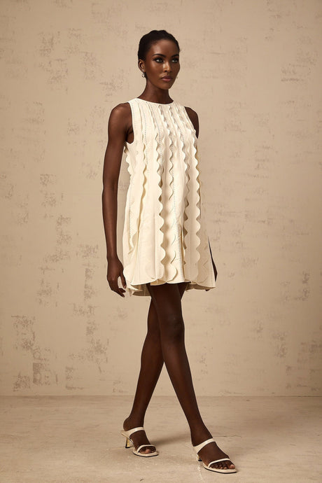 A sleeveless white mini dress with wavy details named Axelle on a plain background