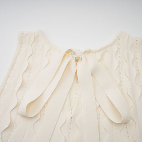 A sleeveless white mini dress with wavy details named Axelle on a plain background