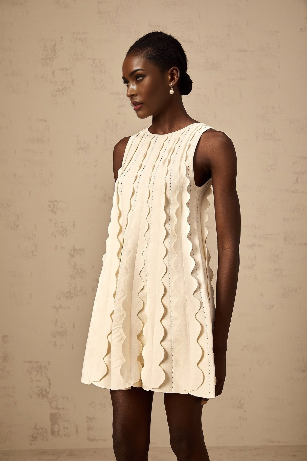A sleeveless white mini dress with wavy details on a female model named Axelle