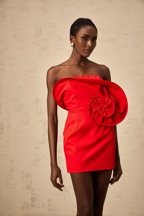 A vibrant red mini dress with an offshoulder neckline featuring a large sculptural rose detail on the bodice creating a dramatic and romantic silhouette