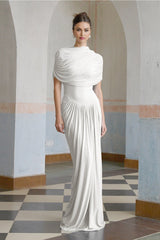 A white asymmetric maxi dress with pleated details and a flowing skirt worn by a model standing against a plain background