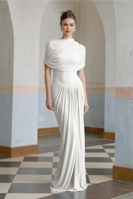 A white asymmetric maxi dress with pleated details and a flowing skirt worn by a model standing against a plain background