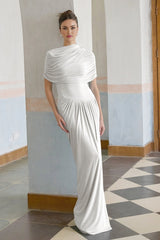 A white asymmetric maxi dress with pleated details featuring a flowing skirt and uneven hemline worn by a female model