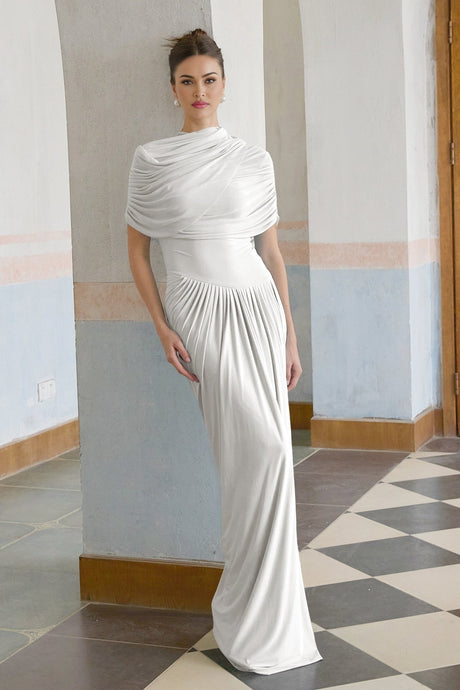 A white asymmetric maxi dress with pleated details featuring a flowing skirt and uneven hemline worn by a female model