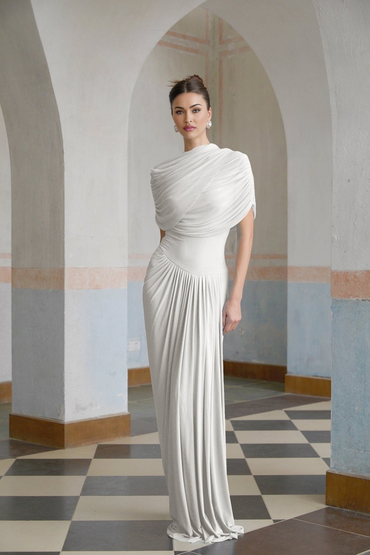 A white asymmetric maxi dress with pleated details featuring a long flowing skirt and an uneven hemline