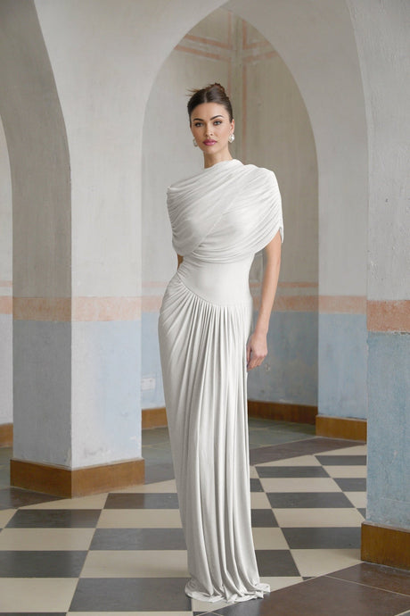 A white asymmetric maxi dress with pleated details featuring a long flowing skirt and an uneven hemline