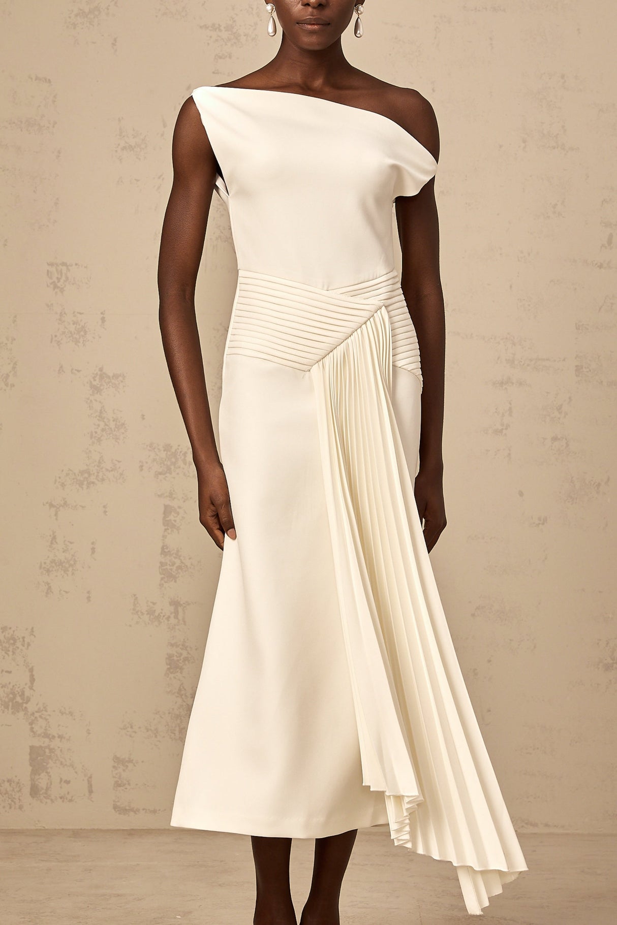 A white asymmetric midi dress with draped fabric details worn by a model standing against a plain background