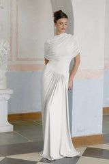 A white asymmetric pleated maxi dress with a flowing silhouette worn by a model standing against a plain background