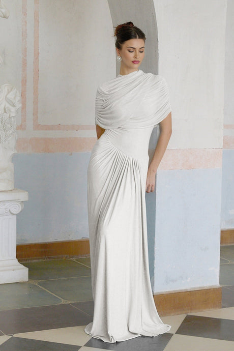 A white asymmetric pleated maxi dress with a flowing silhouette worn by a model standing against a plain background