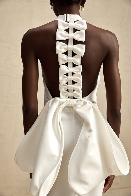A white bandage dress with an oversized bow accent named Capucine featuring a formfitting silhouette and elegant design