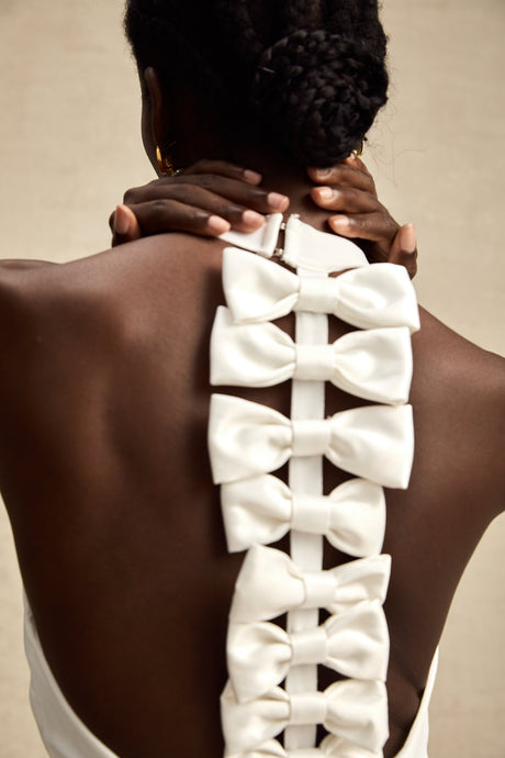 A white bandage dress with an oversized bow detail named Capucine featuring a formfitting silhouette and sleeveless design