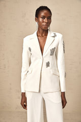 A white blazer and trouser set embellished with crystal details featuring a fitted jacket and matching pants