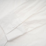 A white buttonup shirt with floral cutout patterns visible on the sleeves and body featuring a relaxed fit and collar