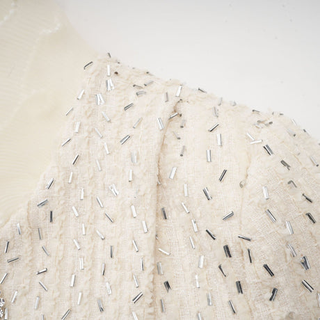 A white cropped jacket with beaded details and ruffle trim featuring short sleeves and an open front design