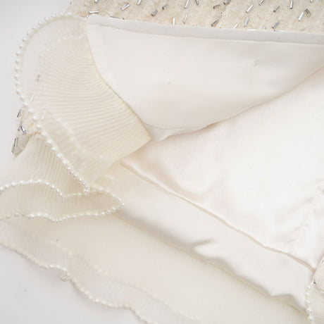 A white cropped jacket with beaded embellishments and ruffle details along the edges