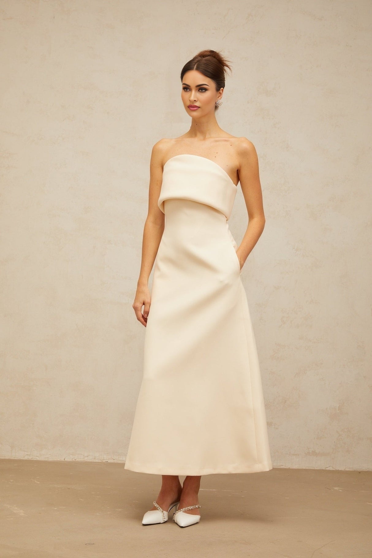 A white folded corset midi dress with a fitted bodice and flared skirt hanging on display