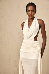 A white halterneck maxi dress with a backless design featuring a flowing long skirt and sleeveless style