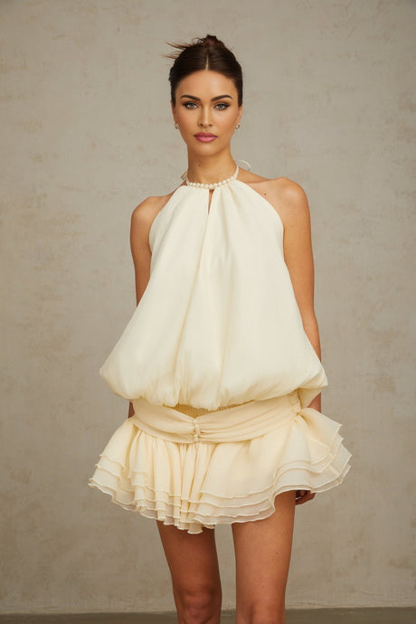 A white halterneck mini dress with faux pearl embellishments on a model named Berenice