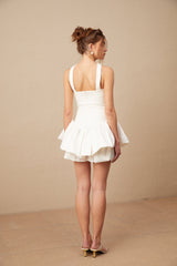 A white halterneck mini dress with ruffled details called Olivia worn by a female model against a plain background