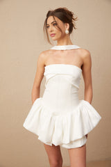 A white halterneck mini dress with ruffled details modeled by a woman named Olivia