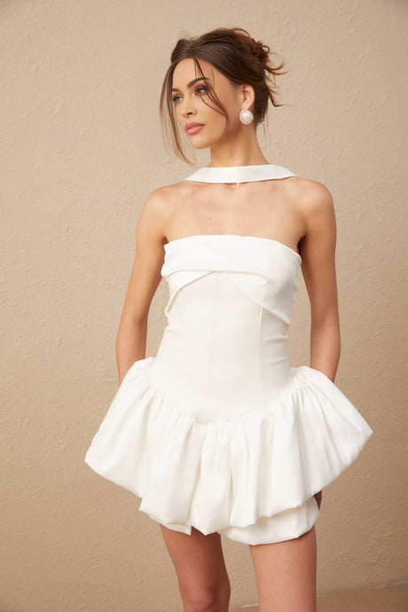 A white halterneck mini dress with ruffled details modeled by a woman named Olivia