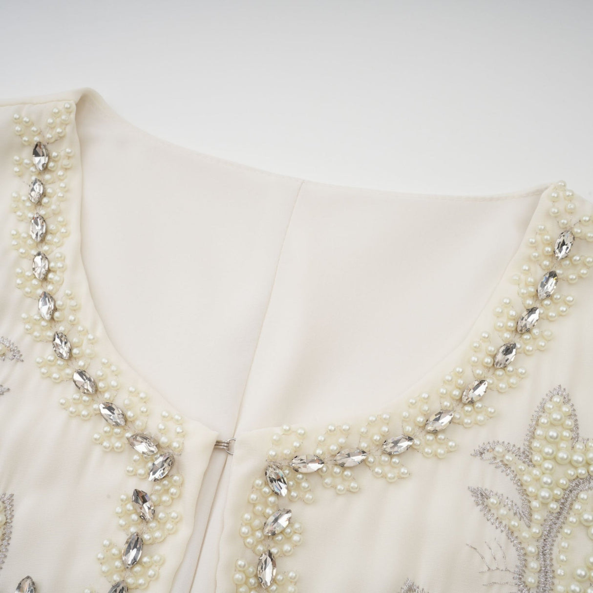 A white jacket and dress set featuring embellishments and pleats The jacket has a cropped design while the dress is sleeveless with a fitted bodice and flared skirt Both pieces are adorned with delicate embroidery or beadwork for an elegant formal look