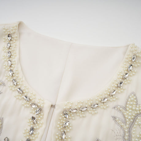 A white jacket and dress set featuring embellishments and pleats The jacket has a cropped design while the dress is sleeveless with a fitted bodice and flared skirt Both pieces are adorned with delicate embroidery or beadwork for an elegant formal look