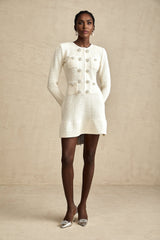 A white knitted mini dress with a flared skirt and short sleeves on a female model against a plain background
