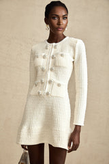 A white knitted mini dress with a flared skirt and short sleeves worn by a model standing against a plain background