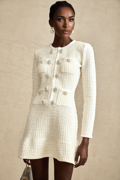 A white knitted mini dress with a flared skirt and short sleeves worn by a model standing against a plain background