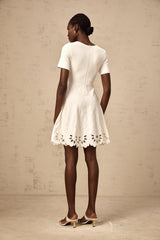 A white knitted mini dress with cut out details and jacquard pattern worn by a model standing against a plain background