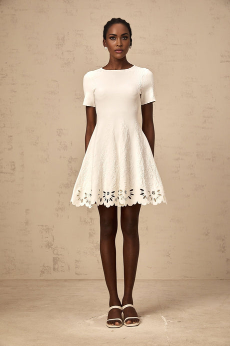 A white knitted mini dress with cutout jacquard pattern worn by a model standing against a plain background