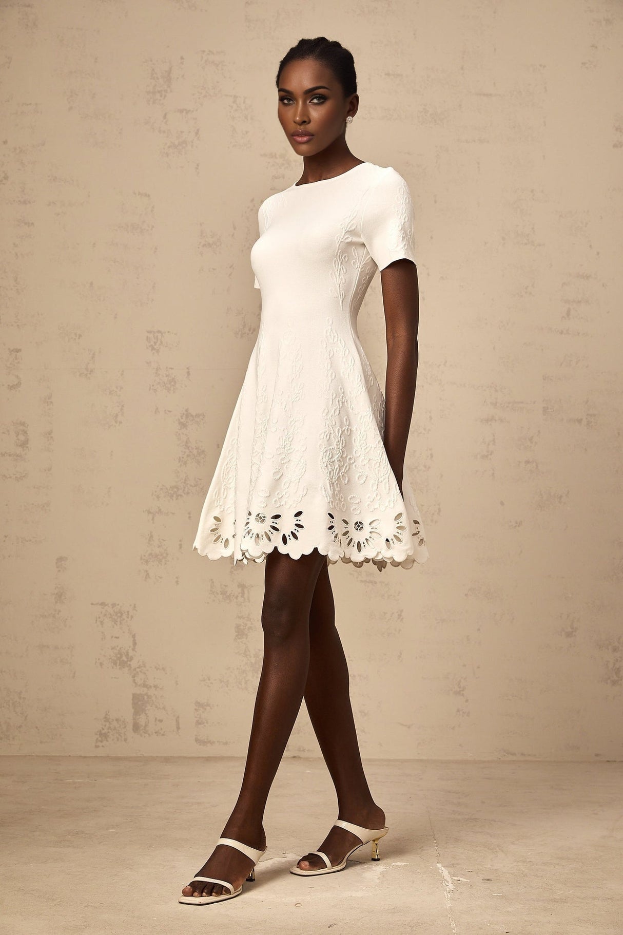 A white knitted mini dress with jacquard pattern and cutout details worn by a model named Émilie
